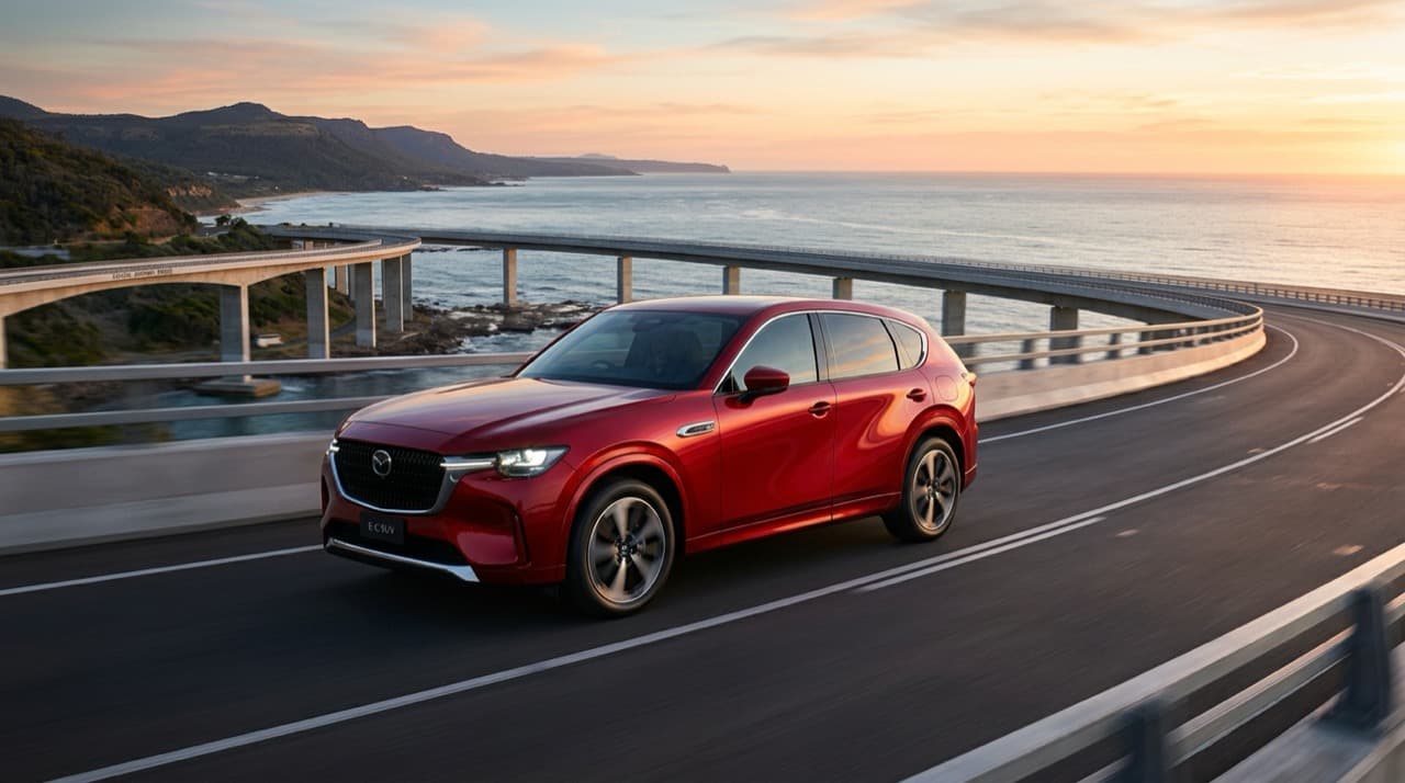 ภาพรถยนต์ไฟฟ้า C-SUV Mazda CX-6e สีแดง Soul Red Crystal ขับเคลื่อนบนสะพานโค้งเลียบทะเล ดีไซน์ Kodo ปราดเปรียวและไฟหน้า LED เฉียบคม